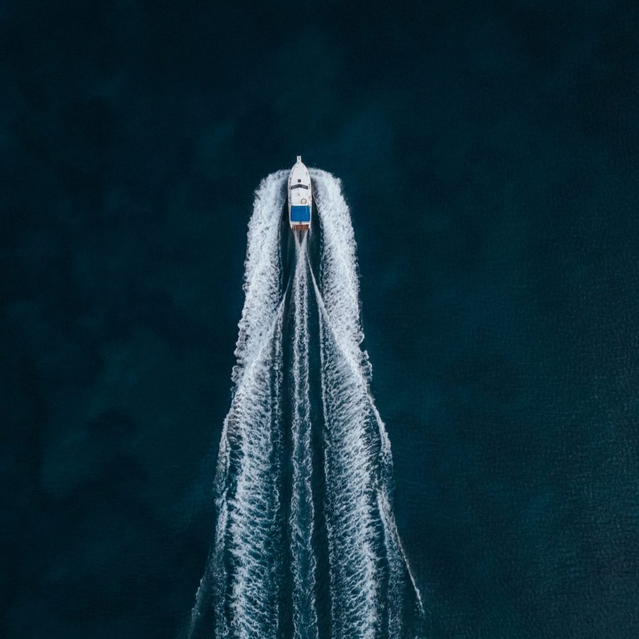 Aerial overhead shot of a motorboat sailing forward in the middle of the ocean An aerial overhead shot of a motorboat sailing forward in the middle of the ocean